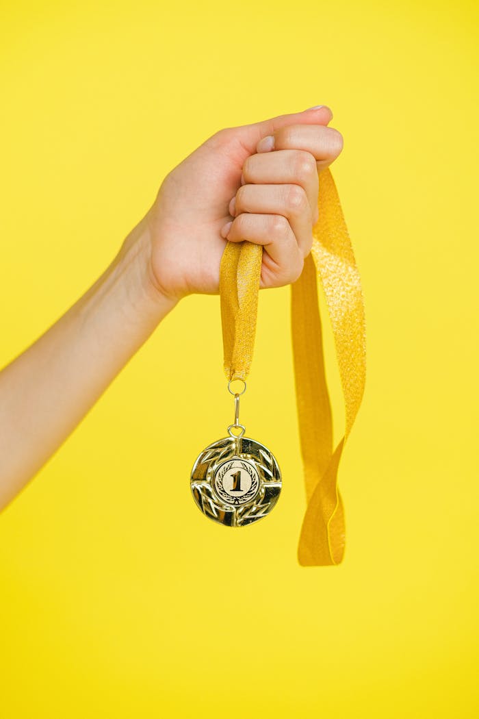 Close-up of a hand holding a gold medal symbolizing achievement and success.